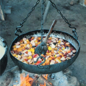 Über einem Lagerfeuer hängt ein eiserner Kessel. Darin kocht eine Suppe aus verschiedenfarbigen Früchten. Ein Holzlöffel zum Umrühren ist auf den Rand des Kessels gelegt. (© LAKD M-V/LA)