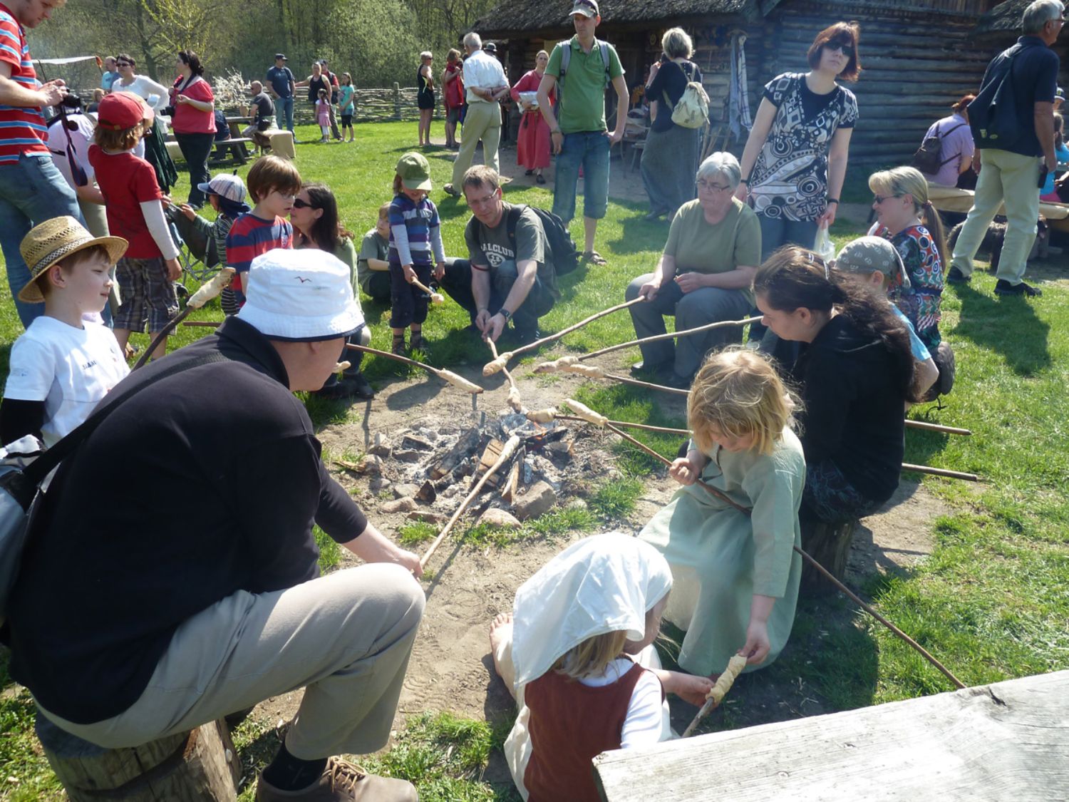 An einem Lagerfeuer sitzt eine Gruppe von Kindern und Erwachsenen. Sie halten Teig an langen Stäben über das Feuer. (© LAKD M-V/LA)