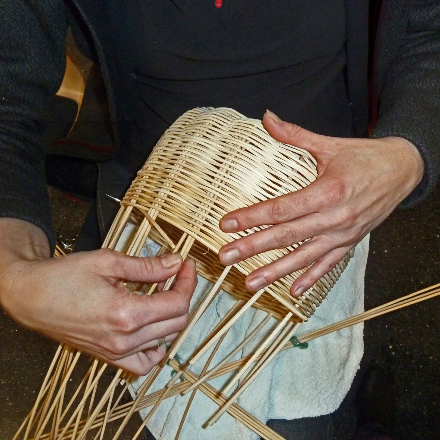 In kleiner Runde Handwerkstechniken lernen und ausprobieren: Das bieten die Workshops. (© LAKD M-V/LA) Eine Frau hält einen Korb auf ihrem Schoß. Der Korb ist noch nicht fertig. Mit ihren Händen flicht sie aus feinen Zweigen das Oberteil des Korbes. (© LAKD M-V/LA)