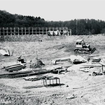 In einer Senke liegt und steht Baumaterial. Dazwischen fährt eine Planierraupe herum. Im Hintergrund wird ein Gerüst aus Holzlatten gebaut. (© LAKD M-V/LA)