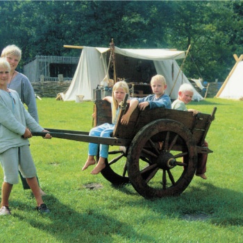 Drei Kinder sitzen auf einem zweirädrigen Wagen mit Speichenrädern. Zwei andere Kinder ziehen den Wagen. (© LAKD M-V/LA)