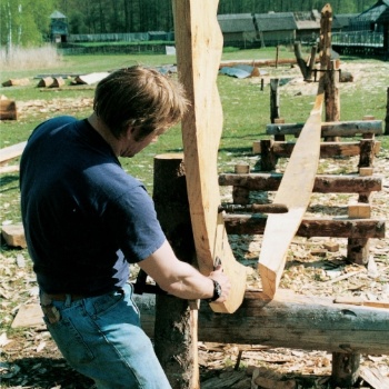 Ein Mann fügt zwei große Holzteile zusammen, die auf einem Gerüst aus Holzstämmen liegen. (© LAKD M-V/LA)