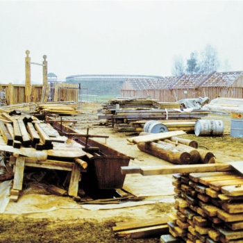 Im Vordergrund liegen Holzstapel, Fässer und anderes Baumaterial. Im Hintergrund stehen die hölzernen Gerüste mehrerer Häuser. (© LAKD M-V/LA)